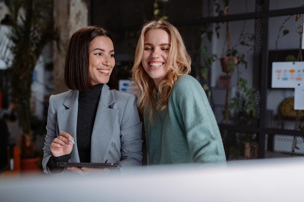 Des femmes heureuses du millénaire distraites du travail sur l'ordinateur en train de discuter au bureau pendant les pauses.