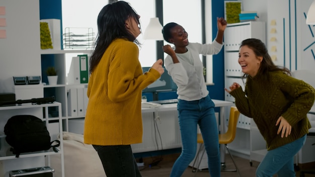 Femmes heureuses de race mixte dansant joyeusement dans le bureau de l'agence de création de démarrage