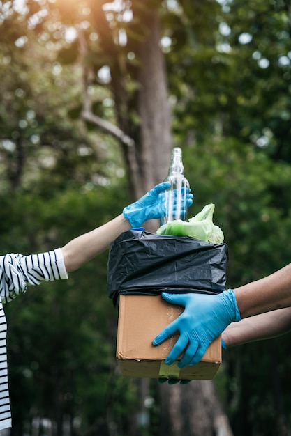 Des femmes et des hommes stockent des bouteilles de déchets en plastique dans des sacs noirs au parc à la lumière du matin