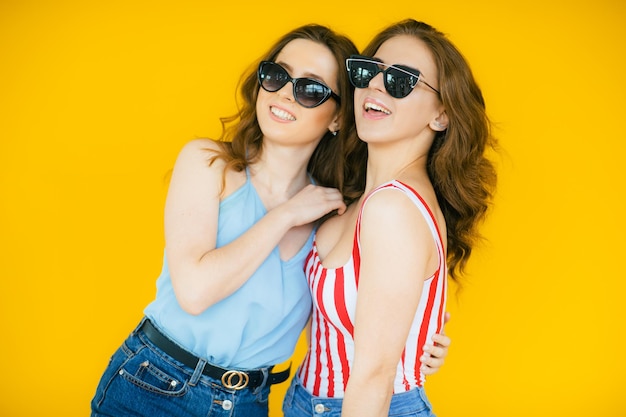 Femmes insouciantes sexy posant près du mur jaune dans des lunettes de soleil Modèles positifs allant