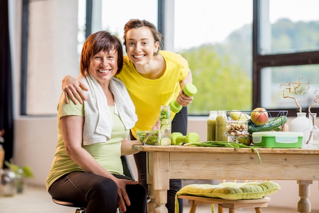 Femmes jeunes et plus âgées faisant de l'exercice avec des haltères et mangeant des aliments sains à l'intérieur sur le fond de la fenêtre
