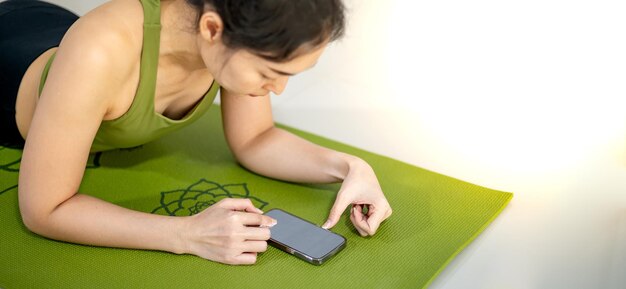 Des femmes jouant au mobile et assises sur le tapis de yoga vert tout en se reposant pour une pratique à la maison