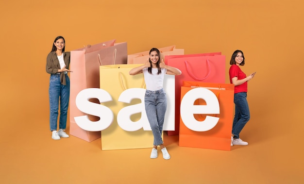 Des femmes latines avec un téléphone font du shopping près de grands sacs à fond orange.