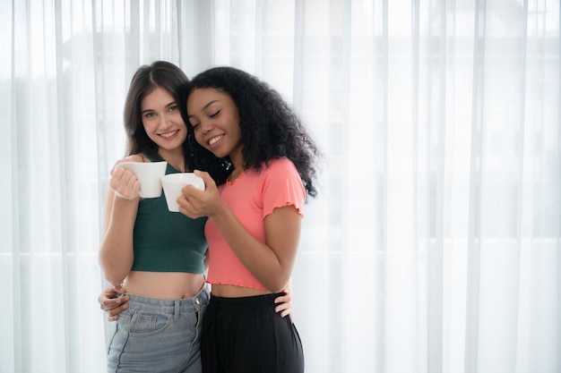 Femmes lesbiennes souriantes avec des drapeaux arc-en-ciel assis sur le lit dans la chambre à la maison