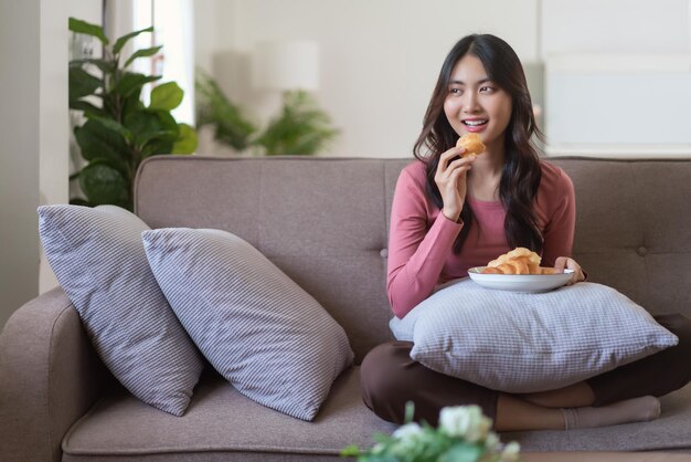 Les femmes loisirs sur le canapé pour manger du pain et regarder dehors profitent d'un style de vie de rêve à la maison