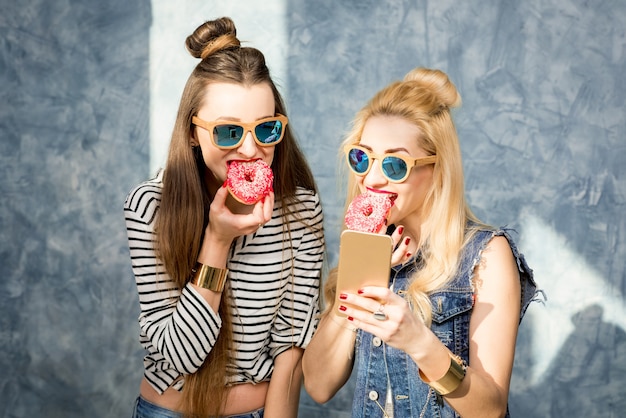 Femmes ludiques s'amusant avec des beignets sucrés sur fond de mur bleu