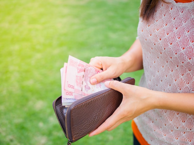 Photo femmes mains prenant de l'argent thai baht du portefeuille sur le terrain d'herbe verte.