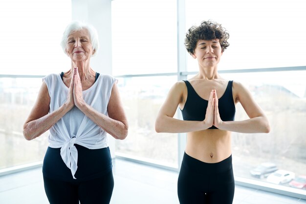 Femmes méditant et faisant du yoga à côté d'une grande fenêtre