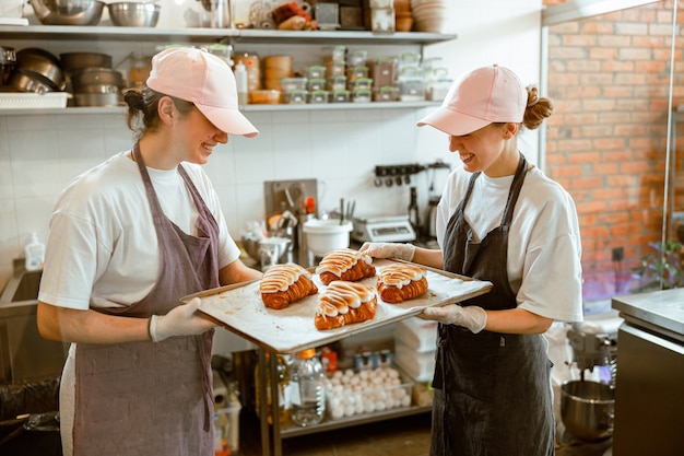 Les femmes pâtissières tiennent un grand plateau avec des croissants décorés dans une boulangerie