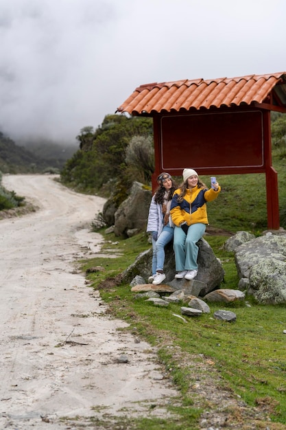 Femmes prenant un selfie assis sur un rocher à côté d'un arrêt de bus dans la montagne