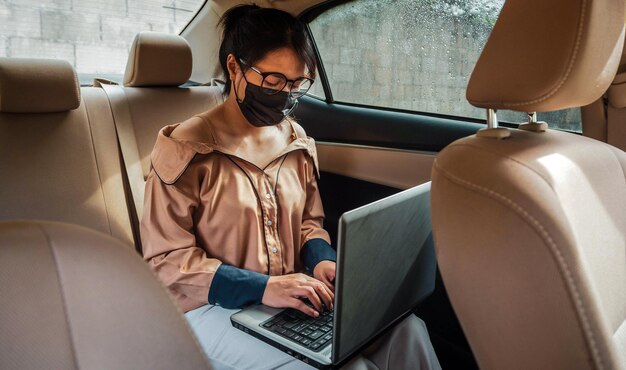 Les femmes qui travaillent assis à l'arrière d'une voiture portant un masque de protection et travaillant à un ordinateur