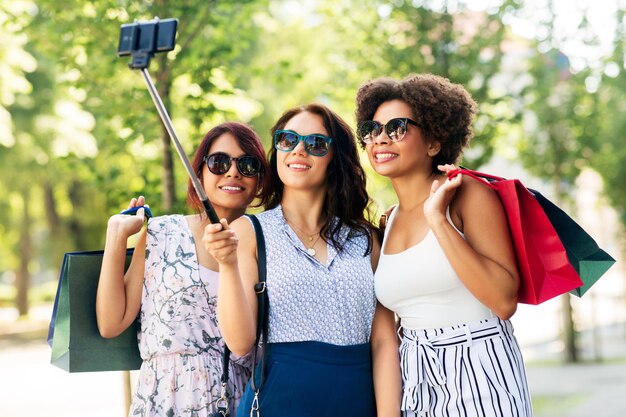 Des femmes avec des sacs d'achat se faisant des selfies à l'extérieur.