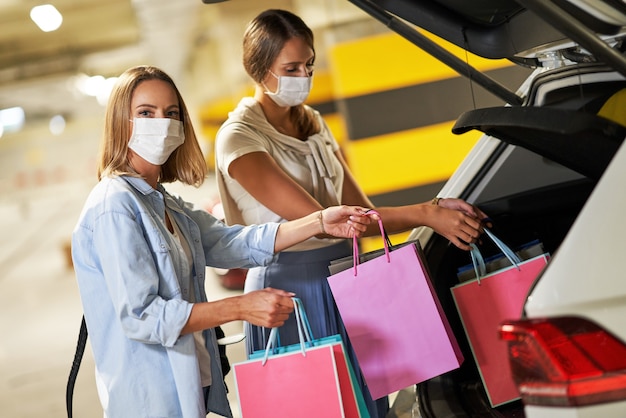 femmes avec des sacs à provisions dans des masques dans un parking souterrain