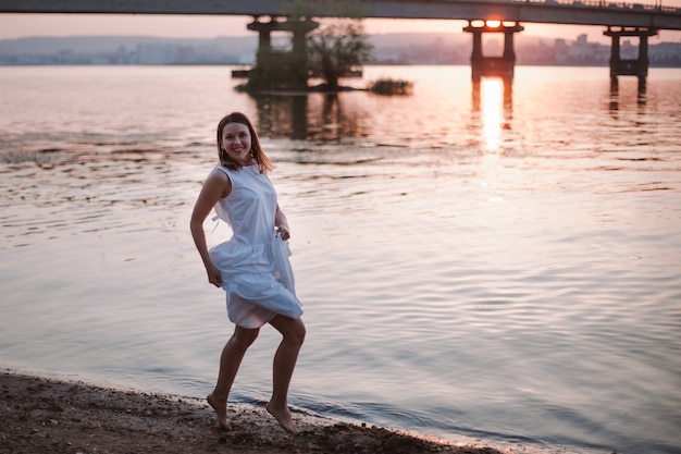 Les femmes sautant au coucher du soleil une femme joyeuse qui rit dans une robe d'été blanche passe un bon moment sur t ...