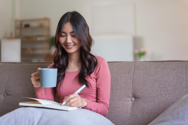 Les femmes se divertissent sur le canapé pour boire du café et écrire des notes sur un carnet de notes dans un style de vie à la maison