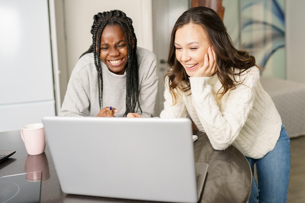 Photo des femmes souriantes regardant leur ordinateur portable à la maison.