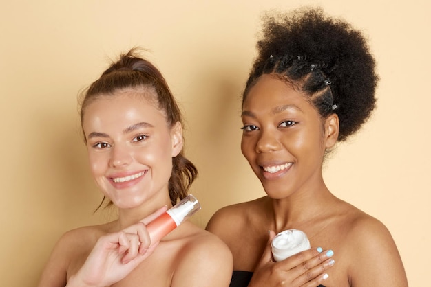 Des femmes souriantes tiennent un pot d'hydratant cosmétique ou un masque facial Photo de jolies femmes multiethniques avec un maquillage parfait sur fond beige Concept de beauté