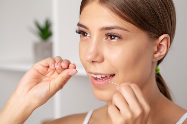 Les femmes souriantes utilisent du fil dentaire blanc dents saines