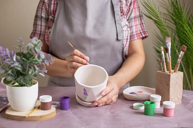 Des Femmes En Tablier Gris Peignent Un Pot En Céramique à Fleurs Blanches