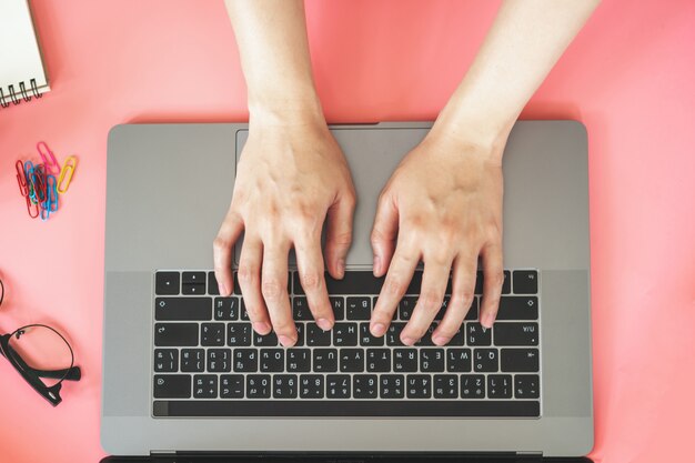 Femmes tapant sur un ordinateur portable dans un bureau coloré pastel rose avec accessoires