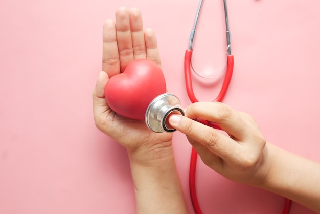 femmes tenant coeur rouge et stéthoscope sur rose