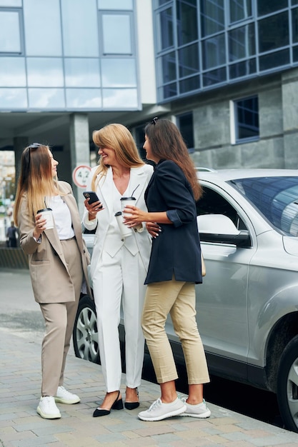 Les femmes en tenue de soirée sont à l'extérieur dans la ville, debout près d'une voiture argentée