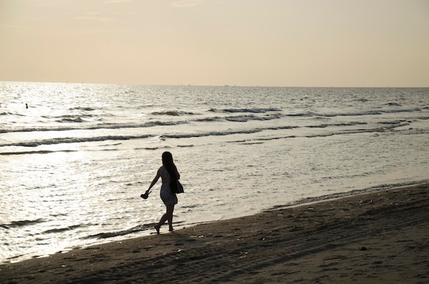 Des femmes thaïlandaises voyageuses marchant seules se sentant seules sur la plage avec le vent et les vagues à la plage de Bangsaen au crépuscule à Chonburi en Thaïlande