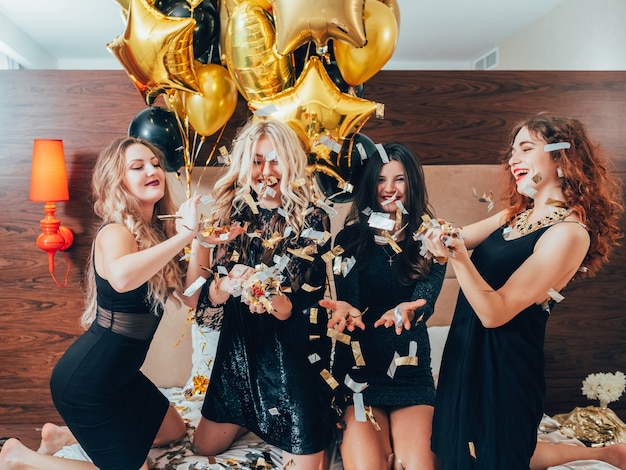 Femmes urbaines. Glamour et style de vie de luxe. Fête. Rangée de jeunes femmes joyeuses se détendre sur le lit. Intérieur de la chambre d'hôtel.