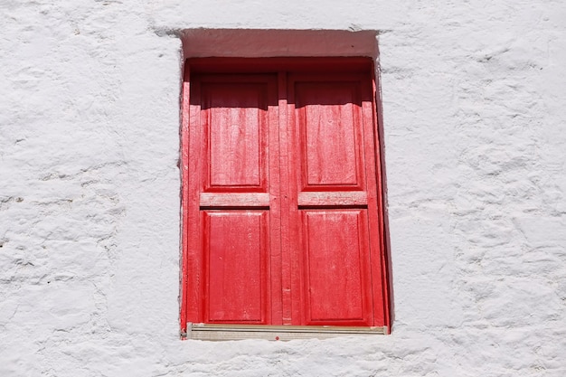 Fenêtre aux volets fermés rouge vif sur un mur blanc