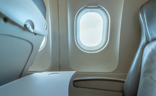 Fenêtre d'avion avec lumière du soleil blanche. Siège en cuir de l'avion de classe économique.