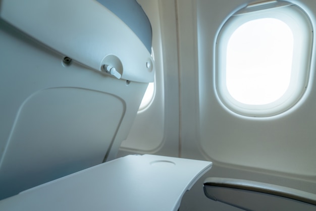 Fenêtre d'avion avec lumière du soleil blanche. Table de plateau d'avion en plastique vide à l'arrière du siège. Fenêtre d'avion en classe économique.