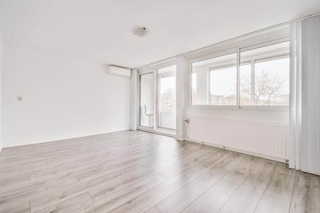 Fenêtre de balcon en plastique et radiateur sur mur blanc avec parquet dans une pièce lumineuse vide à la maison