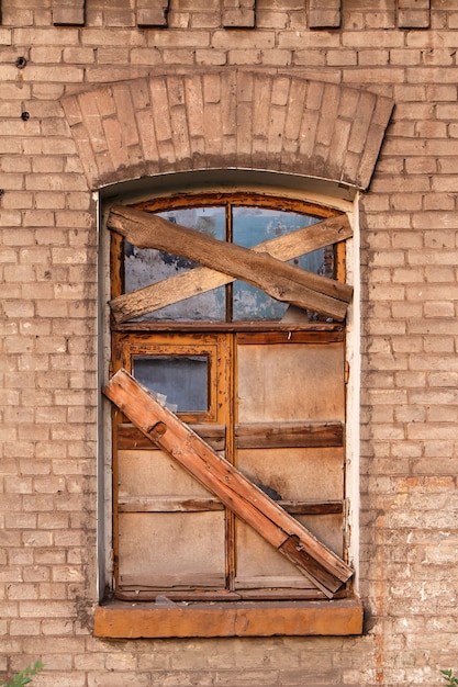 Fenêtre bordée de planches de bois dans un ancien bâtiment en brique abandonné