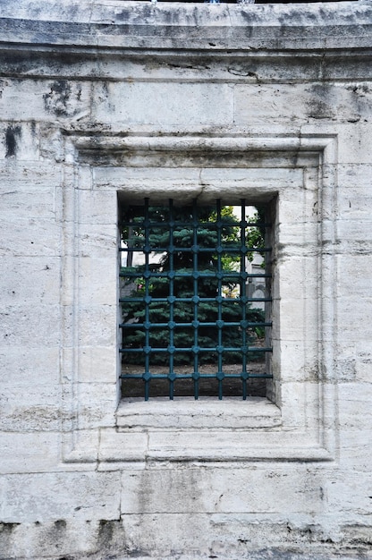 Fenêtre carrée à barreaux. Une fenêtre dans le mur d'une vieille maison sans verre. Grille en métal forgé sur la fenêtre.