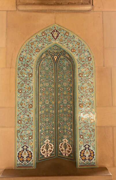 Une fenêtre décorative dans un mur de pierre avec un carreau bleu et vert avec le mot qabra dessus.