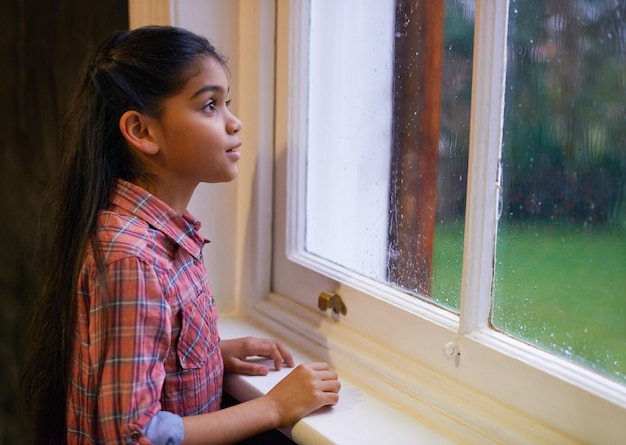 Fenêtre de pluie et fille avec des idées pensant ou émerveillant avec des pensées méditer ou enfant à la maison Personne de sexe féminin enfant pensif et modèle avec maison de temps d'hiver et tempête avec fantaisie et verre torride