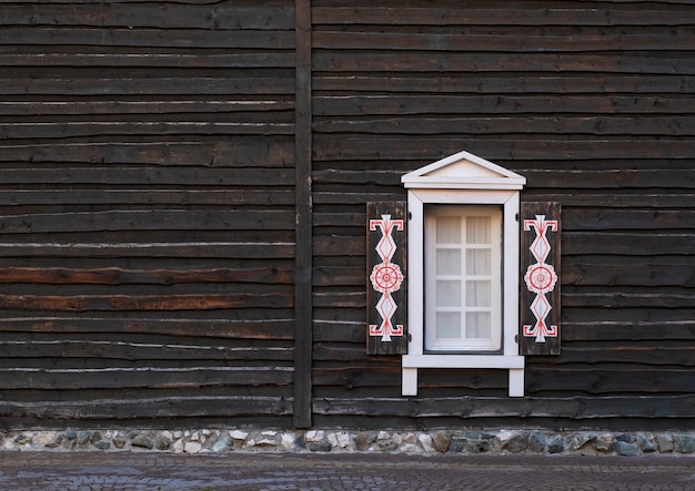 Photo fenêtre sculptée antique sur façade en bois sombre.
