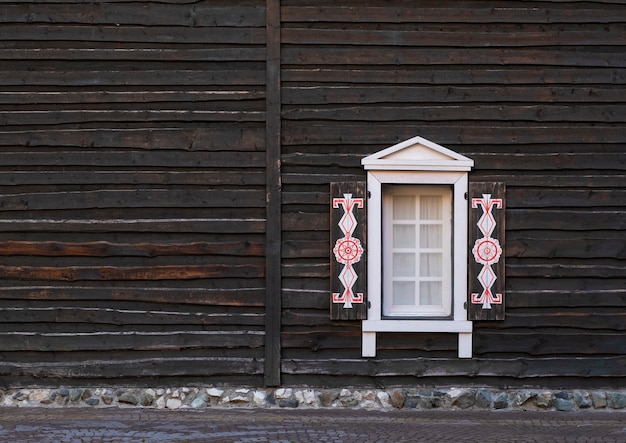 Fenêtre sculptée antique sur façade en bois sombre.