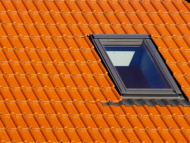 Fenêtre sur le toit de la maison avec des tuiles orange sur fond de ciel bleu
