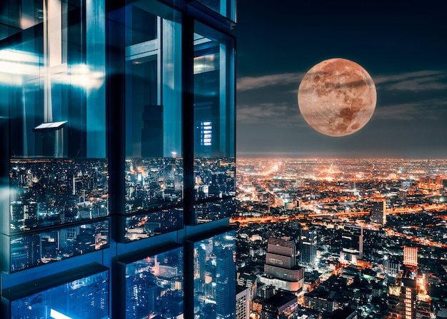 Fenêtre en verre faisante le coin du gratte-ciel avec la super lune rougeoyante sur la ville illuminée à Bangkok