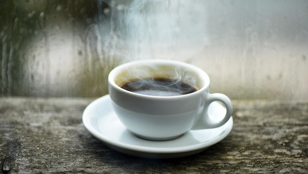 Fenêtre en verre humide et tasse de café chaud. Le temps nuageux d'automne est meilleur avec une boisson à la caféine. Bénéficiant d'un café un jour de pluie. L'heure du café un jour de pluie. Café fraîchement moulu dans une tasse ou une tasse blanche sur le rebord de la fenêtre.