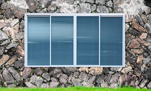 Fenêtre en verre moderne sur le mur de pierre et le cadre de fenêtre de grassblanket vert