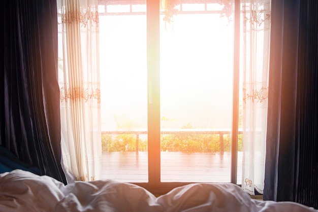 Fenêtre vue nature montagne verte dans le lit à la chambre matin et lumière du soleil - vitre avec draperie