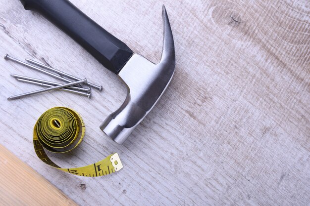 Fer à marteau, ruban centimétrique et clous sur table en bois