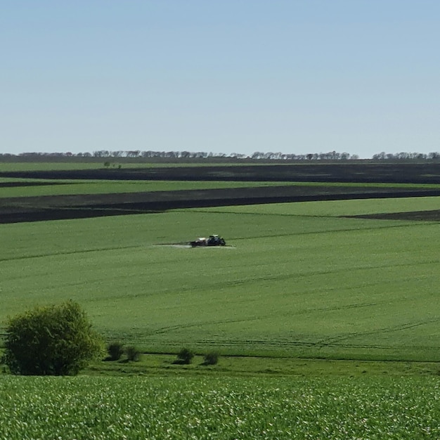 Une ferme est au loin avec un tracteur au milieu.