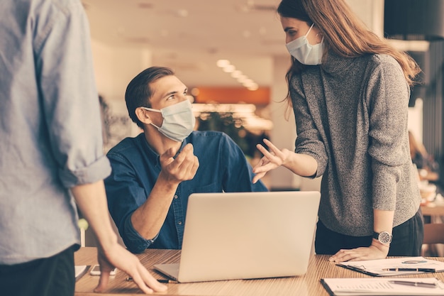 Fermer. employés portant des masques de protection discutant de problèmes de travail.