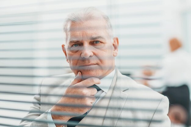 Fermer. homme d'affaires âgé maussade debout devant la fenêtre du bureau.