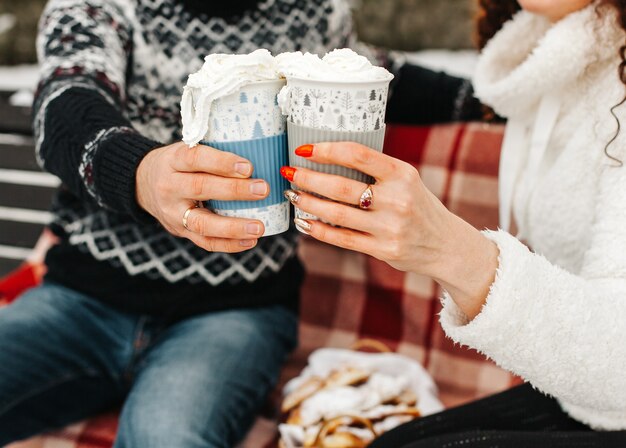 Fermer. homme et femme tenant des tasses de chocolat chaud avec de la crème dans la forêt d'hiver