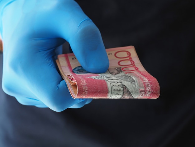 Fermer. Homme en gants bleus détient des billets en argent pesos République dominicaine.