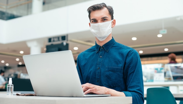 Fermer. homme sérieux dans un masque de protection assis à un bureau. concept de protection de la santé